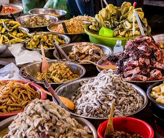 Kamboçya Mutfağı Kamboçya, Güneydoğu Asya’da Mekong Nehri ve Tonle Sap Gölü’nün kesişim noktasında yer alır. Bu stratejik konum, Kamboçya mutfağının hem Çin hem de Tayland mutfaklarından etkilenmesine olanak tanımıştır. Pirinç ve balık, mutfağın temel öğelerini oluştururken, taze otlar ve baharatlar yemeklere karakter kazandırır. Kamboçya mutfağı, hem geleneksel hem de modern öğeleri harmanlayarak zengin bir lezzet deneyimi sunar. Konulu bir haber görseli.