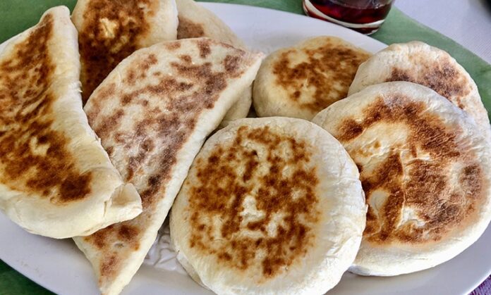 Bazlama Gelenekten Sofralara Uzanan Sıcak Lezzet Türk mutfağının en özel ve sevilen ekmek çeşitlerinden biri olan bazlama, yumuşak dokusu, doyurucu yapısı ve mis gibi kokusuyla sofraların vazgeçilmezidir. Özellikle Anadolu’nun birçok bölgesinde kahvaltıların, çay saatlerinin ve hatta ana yemeklerin yanında sıklıkla tercih edilen bu ekmek, sadece lezzetiyle değil kültürel bir değer olarak da öne çıkar. Günümüzde modern sofralarda da kendine yer bulan bazlama, hem geleneksel hem de pratik bir lezzet olarak dikkat çekmektedir. Konulu bir haber görseli.