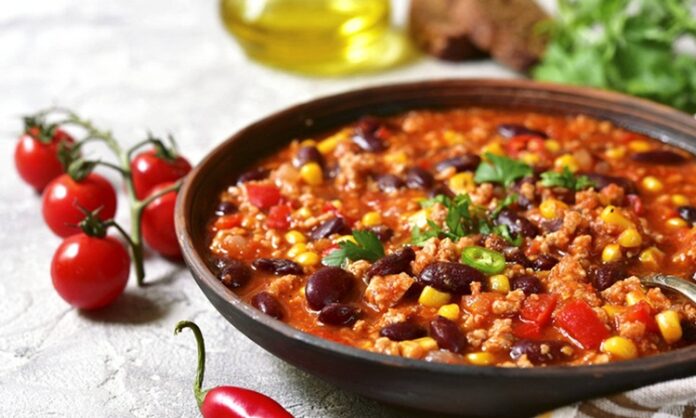 Chili Con Carne, Meksika ve Amerika mutfaklarının kesişim noktasında doğmuş, dünya genelinde tanınan baharatlı bir yemektir. İsminin anlamı “etli biber” olup, temelinde kırmızı biber ve dana eti yer alır. Kökeni konusunda farklı tartışmalar bulunsa da genellikle Meksika kökenli olduğu kabul edilir. Ancak Texas mutfağının da bu yemeğin yaygınlaşmasında büyük payı vardır. Konulu bir haber görseli.