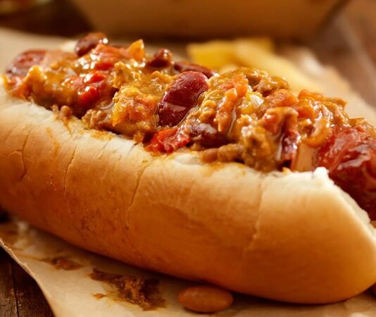 Chili Dog: Sokak Lezzetlerinin Baharatlı Yıldızı Amerika mutfağının en sevilen sokak lezzetlerinden biri olan chili dog, klasik hot dog’un baharatlı bir versiyonudur. Kökeni 20. yüzyılın başlarına uzanan bu yiyecek, özellikle Teksas ve Kaliforniya sokaklarında popüler hale gelmiştir. Klasik sosis ve ekmek kombinasyonunun üzerine eklenen acılı chili sos, chili dog’un karakteristik özelliğini oluşturur. Konulu bir haber görseli.