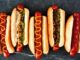Dünya mutfağında geniş bir yer edinen hot dog, özellikle Amerika Birleşik Devletleri’nde adeta bir sembol haline gelmiştir. Kökeni 19. yüzyılın sonlarına kadar uzanan bu yiyecek, Almanya’dan Amerika’ya göç edenlerin beraberinde getirdiği sosis kültürü ile ortaya çıkmıştır. Uzun ekmek arasına yerleştirilen sosisin seneler içinde farklı soslarla buluşması, hot dog’u bugünkü popüler formuna kavuşturmuştur. Konulu bir haber görseli.