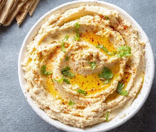 Humus: Lezzetiyle Sofraların Vazgeçilmez Mezesi Humus, Orta Doğu mutfağının en bilinen ve sevilen mezelerinden biridir. Başlıca malzemeleri nohut, tahin, limon suyu, sarımsak ve zeytinyağı olan bu özel tarif, yüzyıllardır sofralarda yerini almaktadır. Tarihi çok eski dönemlere dayanan humus, özellikle Lübnan, Suriye, Filistin ve Türkiye gibi bölgelerde yaygın olarak tüketilir. Bugün ise dünya genelinde sağlıklı bir atıştırmalık ya da ana yemek yanında tamamlayıcı olarak tercih edilmektedir. Konulu bir haber görseli.