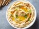 Humus: Lezzetiyle Sofraların Vazgeçilmez Mezesi Humus, Orta Doğu mutfağının en bilinen ve sevilen mezelerinden biridir. Başlıca malzemeleri nohut, tahin, limon suyu, sarımsak ve zeytinyağı olan bu özel tarif, yüzyıllardır sofralarda yerini almaktadır. Tarihi çok eski dönemlere dayanan humus, özellikle Lübnan, Suriye, Filistin ve Türkiye gibi bölgelerde yaygın olarak tüketilir. Bugün ise dünya genelinde sağlıklı bir atıştırmalık ya da ana yemek yanında tamamlayıcı olarak tercih edilmektedir. Konulu bir haber görseli.
