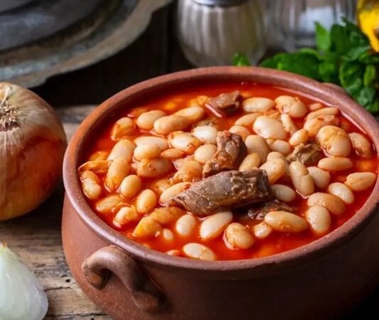 Kuru fasulye, Türk mutfağının en sevilen yemeklerinden biri olarak yüzyıllardır sofralarda yerini koruyor. Geleneksel lezzetlerin başında gelen kuru fasulye, hem doyuruculuğu hem de besleyici özellikleriyle ön plana çıkıyor. Pirinç pilavıyla oluşturduğu klasik ikili, adeta Anadolu sofralarının simgesi haline gelmiş durumda. Günümüzde de hem ev yemeklerinde hem de restoran menülerinde en çok tercih edilen yemeklerden biri olmayı sürdürüyor. Konulu bir haber görseli.