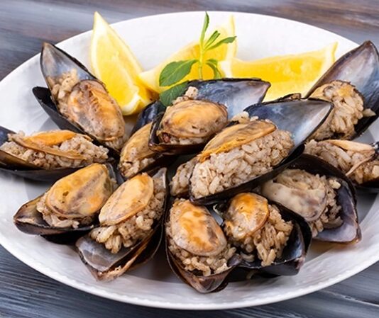 Türk mutfağının en bilinen sokak lezzetlerinden biri olan midye dolma, kökeni Osmanlı dönemine kadar uzanan köklü bir geçmişe sahiptir. Saray mutfağında farklı baharatlarla hazırlanan pirinçli yemeklerin deniz ürünleriyle birleşmesi sonucu ortaya çıktığı düşünülmektedir. Zamanla bu lezzet, sokaklara taşınarak herkesin ulaşabileceği bir hale gelmiştir. Konulu bir haber görseli.