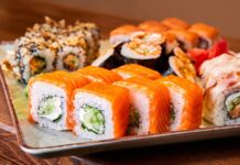 Sushi Roll: Dünyada Popülerliği Artan Japon Lezzeti Sushi roll, Japon mutfağının en bilinen yemeklerinden biridir ve dünya genelinde ün kazanmıştır. İlk olarak Edo döneminde ortaya çıkan sushi, başlangıçta balığın pirinç içinde fermente edilmesiyle hazırlanıyordu. Zaman içinde bu yöntem değişti ve daha modern bir hale geldi. Özellikle 20. yüzyılın ortalarında Amerika’da popülerleşen sushi roll, farklı malzemelerin bir araya gelmesiyle çeşitlenerek bugünkü halini aldı. Konulu bir haber görseli.