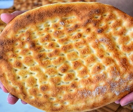 Türk mutfağının en sevilen ekmek çeşitlerinden biri olan tırnak pide, özellikle Ramazan sofralarının ve kebapçıların vazgeçilmez lezzetleri arasında yer alır. Yumuşak içi ve hafif çıtır kabuğu ile öne çıkan bu pide, hem sade olarak hem de farklı yemeklerin eşlikçisi şeklinde tüketilir. Tırnak pide, adını hamura parmak uçlarıyla yapılan tırnak izlerinden alır ve bu izler pişirme sırasında pideye özgün bir görünüm kazandırır. Hem görselliği hem de tadıyla sofraları süsleyen bu geleneksel lezzet, Anadolu’nun mutfak kültüründe önemli bir yere sahiptir. Konulu bir haber görseli.
