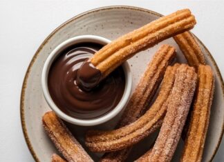 Churros, son yıllarda yalnızca İspanya’nın geleneksel sokak lezzeti olmaktan çıkıp dünya genelinde kafe menülerinin favorisi haline geldi. Özellikle Türkiye’de tatlı kültürünün giderek çeşitlenmesiyle birlikte churros popüler bir alternatif olarak öne çıkıyor. Çıtır yapısı, şeker ve tarçınla kaplanan dış yüzeyi ve sıcak çikolata sosuyla birleştiğinde ortaya çıkan benzersiz tat, birçok insanın yeni gözdesi haline gelmiş durumda. Konulu bir haber görseli.