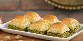 Türkiye’nin en özel tatlılarından biri olan baklava, yüzyıllar boyunca hem coğrafyalara hem de kültürlere yayılan zengin bir mirasa sahip. Orta Asya’dan Anadolu’ya uzanan serüveniyle bugün dünyanın dört bir yanında tanınan bir lezzet hâline gelen baklava, Osmanlı mutfağından itibaren saray sofralarının vazgeçilmez tatlısı olarak kayıt altına alınmıştır. Bu süreçte tatlının yapım teknikleri geliştirilmiş, farklı yörelerde kendine has çeşitleri ortaya çıkmıştır. Gaziantep baklavası, bu tarihsel yolculukta en çok bilinen ve coğrafi işaret tesciline sahip örneklerden biridir. Konulu bir haber görseli.