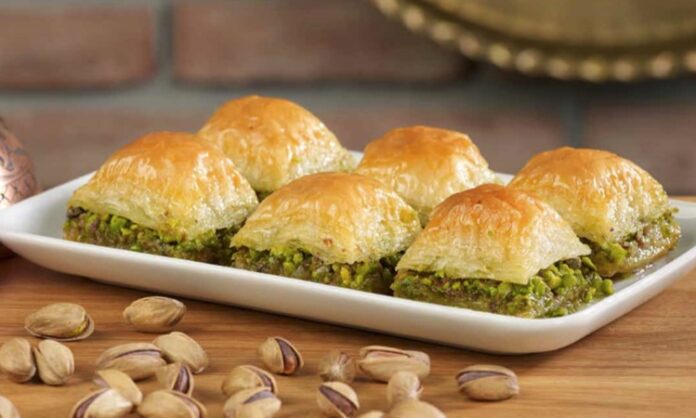 Türkiye’nin en özel tatlılarından biri olan baklava, yüzyıllar boyunca hem coğrafyalara hem de kültürlere yayılan zengin bir mirasa sahip. Orta Asya’dan Anadolu’ya uzanan serüveniyle bugün dünyanın dört bir yanında tanınan bir lezzet hâline gelen baklava, Osmanlı mutfağından itibaren saray sofralarının vazgeçilmez tatlısı olarak kayıt altına alınmıştır. Bu süreçte tatlının yapım teknikleri geliştirilmiş, farklı yörelerde kendine has çeşitleri ortaya çıkmıştır. Gaziantep baklavası, bu tarihsel yolculukta en çok bilinen ve coğrafi işaret tesciline sahip örneklerden biridir. Konulu bir haber görseli.