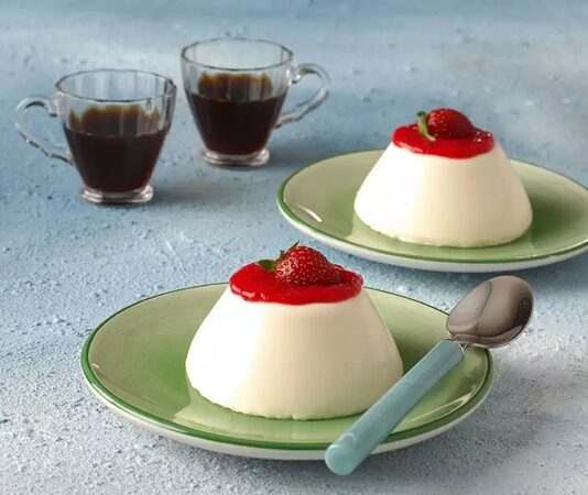 İtalyan mutfağının en rafine tatlılarından biri olan panna cotta, hafif kıvamı, sütlü dokusu ve şık sunumuyla son yıllarda Türkiye’de de oldukça ilgi gören tatlılardan biri hâline geldi. Özellikle yaz aylarında serinletici etkisi nedeniyle tercih edilen bu özel tatlı, hem restoran hem de ev tariflerinde farklı versiyonlarla ortaya çıkıyor. Tatlının temelinde krema bulunması, ona kendine özgü yumuşaklığı kazandırırken, kullanılan vanilya ve meyveler tatlıya zarif bir aroma katıyor. Günümüzde modern pastacılık trendleri sayesinde daha geniş kitlelere ulaşan panna cotta, estetik sunumu ile de dikkat çekiyor. Konulu bir haber görseli.